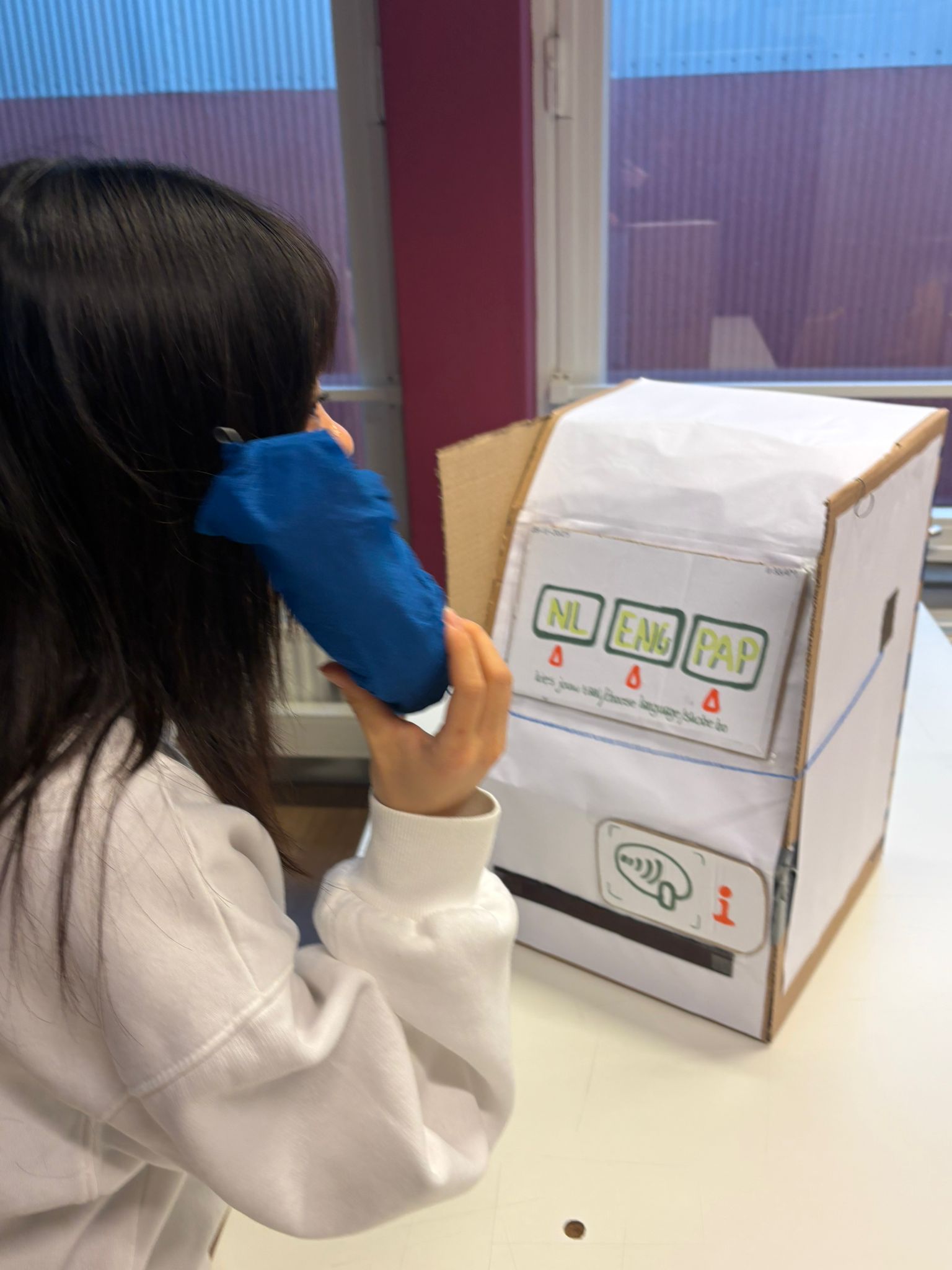 Afbeeldingen van een figuur die bij een kartonnen prototype staat en een telefoon hoorn vast heeft